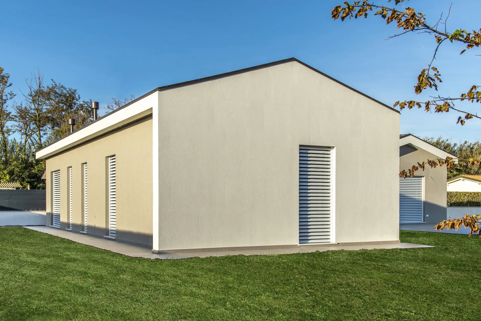 Vista prospettica di una casa in legno prefabbricata con design contemporaneo e finitura esterna pareti ad intonaco in contesto verde di giardino