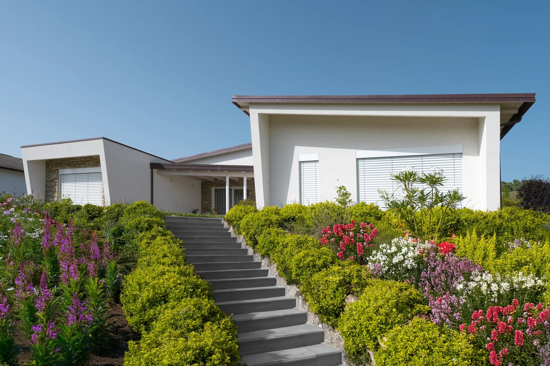 Esterno di una villa in legno in stile contemporaneo, linee pulite, agiardino ben curato e scalinata di accesso a questa esclusiva casa in bioedilizia.